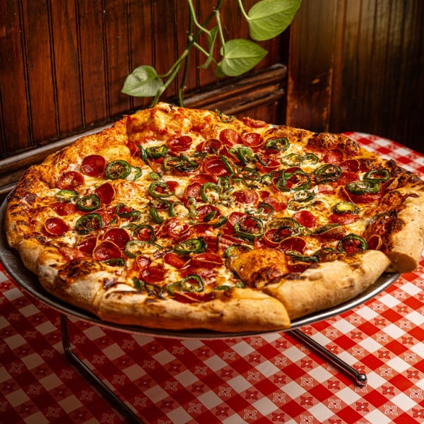 Mattenga's Pizzeria pepperoni and jalapeño pizza on a metal stand over a red and white checkered tablecloth.