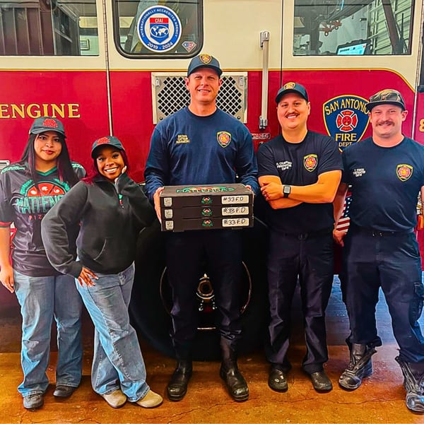 Mattenga's Pizzeria staff delivering pizza boxes to San Antonio firefighters in front of a fire truck.