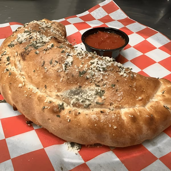 A golden-brown Mattenga's Pizzeria calzone, topped with herbs and cheese, served with a side of marinara sauce.