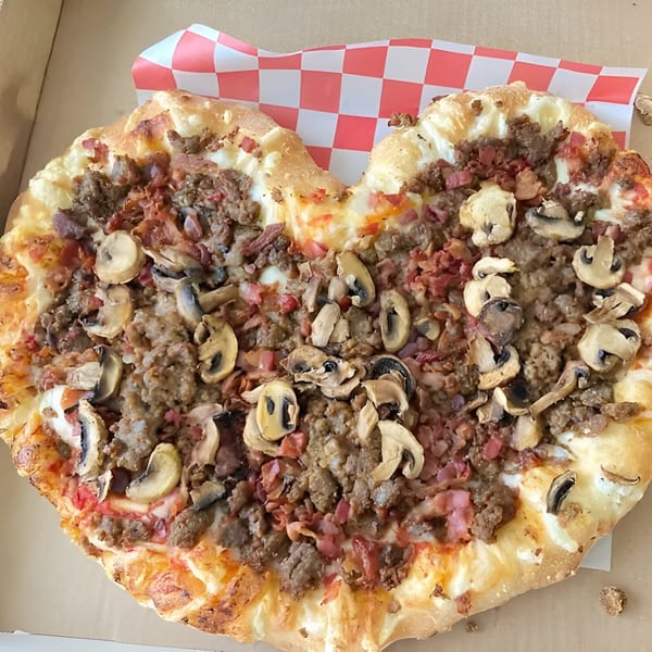 Heart-shaped Mattenga's Pizzeria pizza with sausage, bacon, and mushrooms in a delivery box.