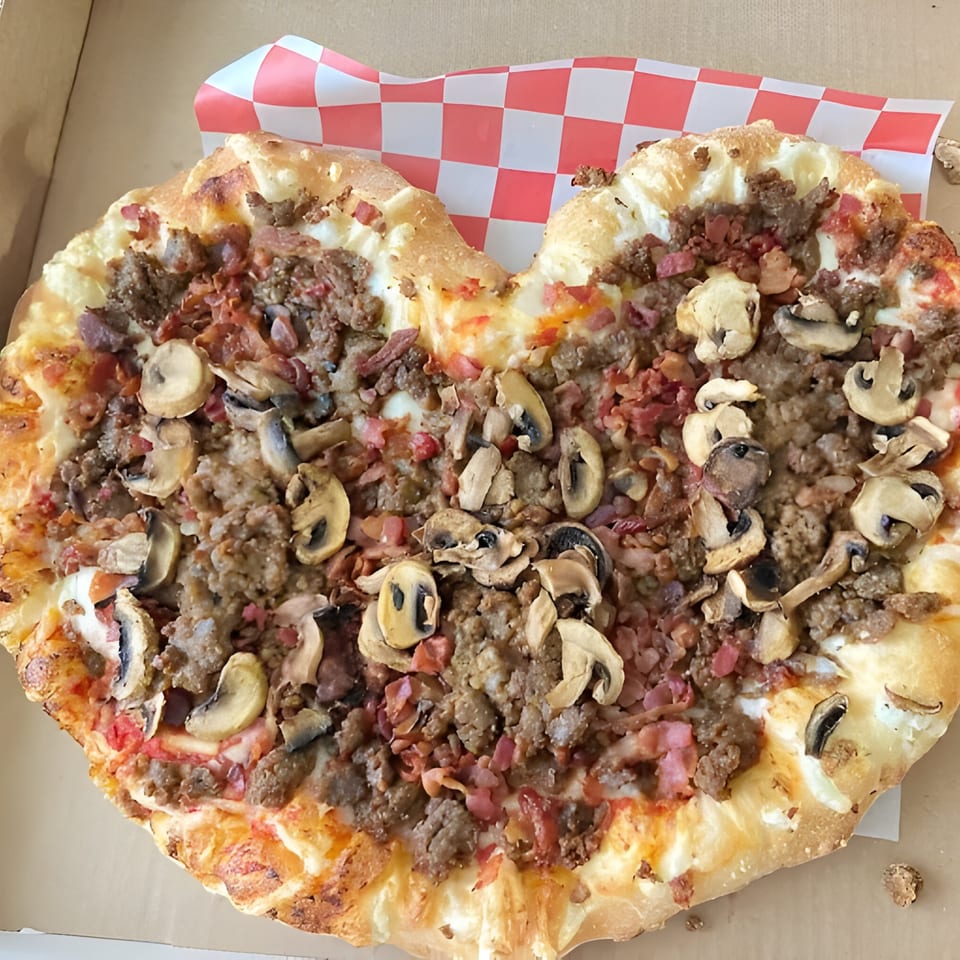 Heart-shaped Mattenga's Pizzeria pizza with sausage, bacon, and mushrooms in a delivery box.