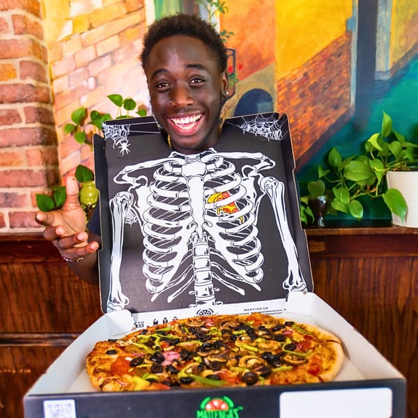 Smiling man in a skeleton pizza box costume holding a Mattenga's Pizzeria pizza.
