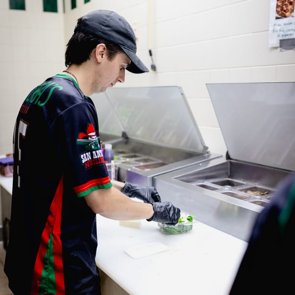 Mattenga's Pizzeria employee in a black and green uniform preparing food behind a counter.