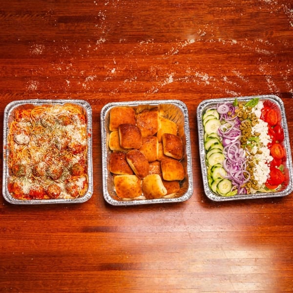 Three catering trays from Mattenga's Pizzeria: spaghetti and meatballs, garlic knots, and a Greek salad.