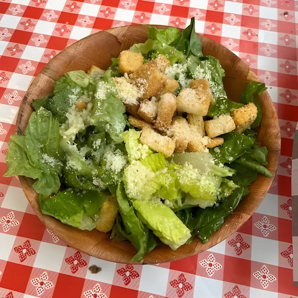 Caesar salad with croutons and parmesan cheese in a wooden bowl on a red and white checkered tablecloth.