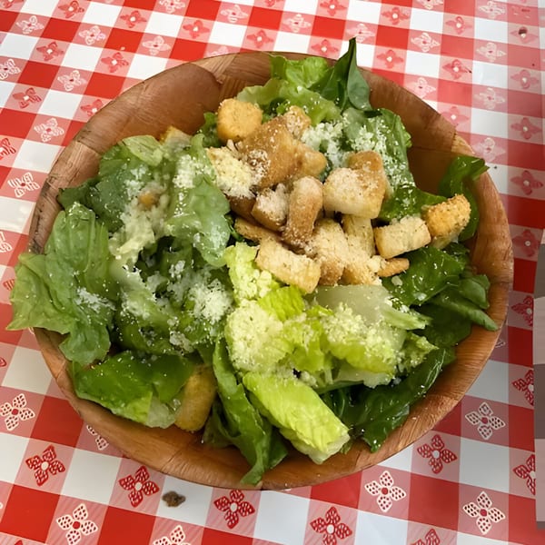 Caesar salad with croutons and parmesan cheese in a wooden bowl on a red and white checkered tablecloth.