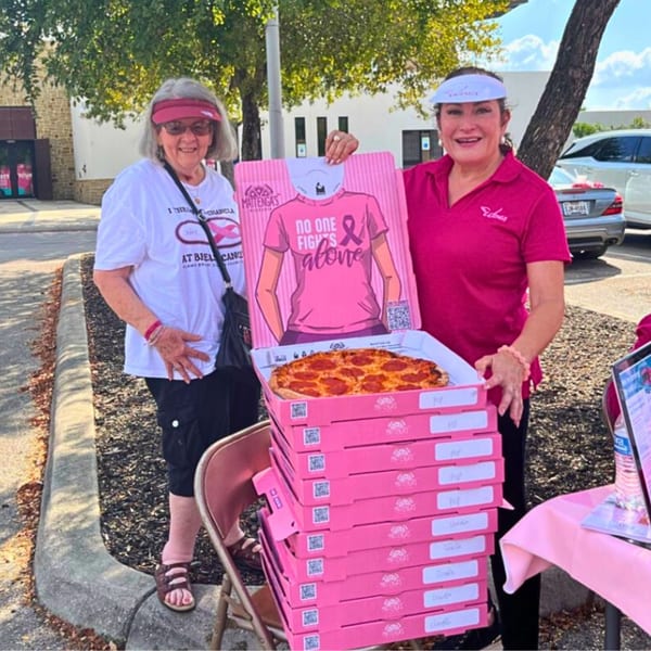 Two women with pink Mattenga's Pizzeria boxes and a pizza, supporting breast cancer awareness.