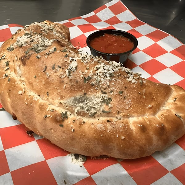 A golden-brown Mattenga's Pizzeria calzone, topped with herbs and cheese, served with a side of marinara sauce.