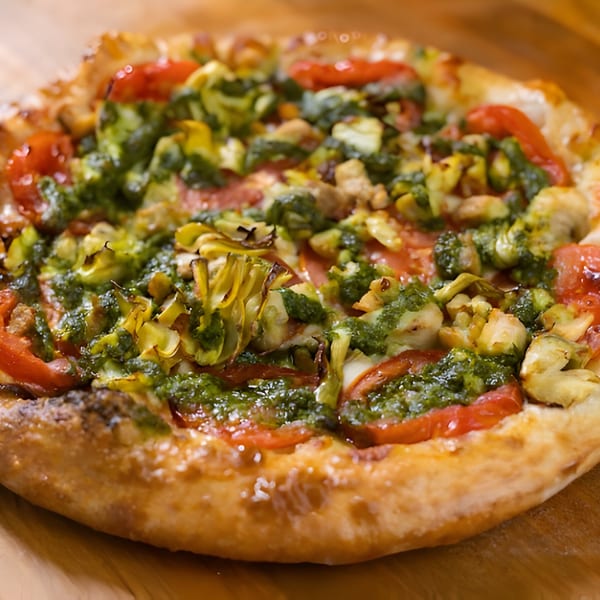 Mattenga's Pizzeria pesto pizza with tomatoes and artichoke hearts on a wooden surface.