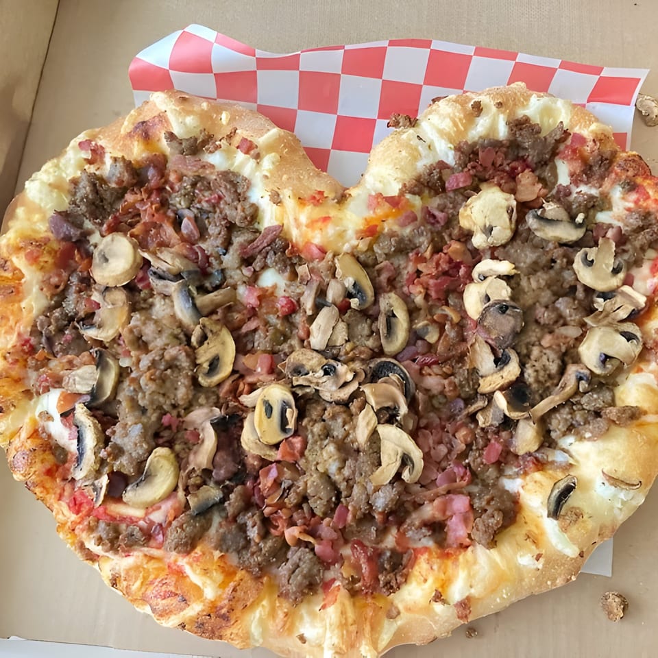 Heart-shaped Mattenga's Pizzeria pizza with sausage, bacon, and mushrooms in a box.