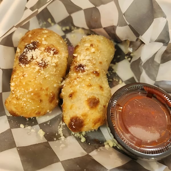 Two golden-brown Mattenga's Pizzeria garlic knots with parmesan cheese, next to a cup of marinara sauce.