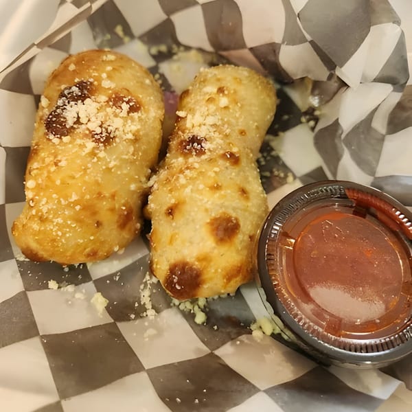 Two golden-brown Mattenga's Pizzeria garlic knots with parmesan cheese, next to a cup of marinara sauce.