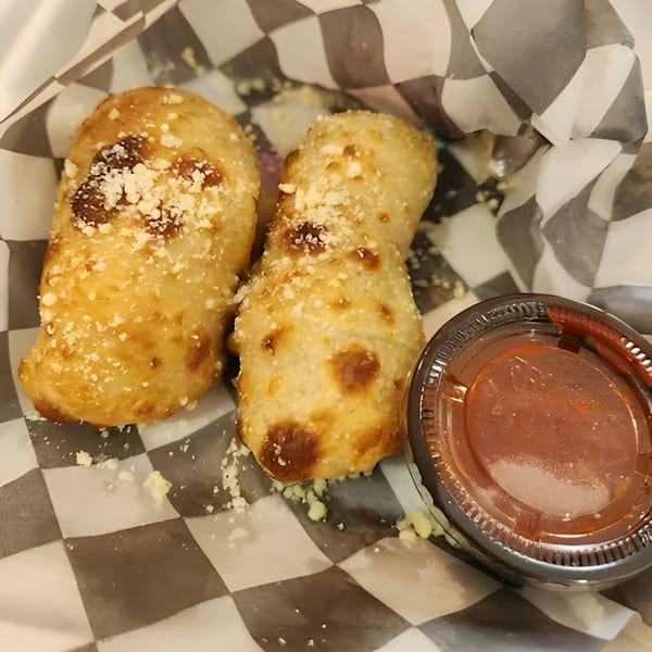 Two golden-brown Mattenga's Pizzeria garlic knots with parmesan cheese, served with a side of marinara sauce.