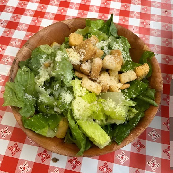 Caesar salad with croutons and parmesan cheese in a wooden bowl on a red and white checkered tablecloth.