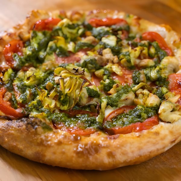 Mattenga's Pizzeria pesto pizza with tomatoes and roasted vegetables on a wooden surface.