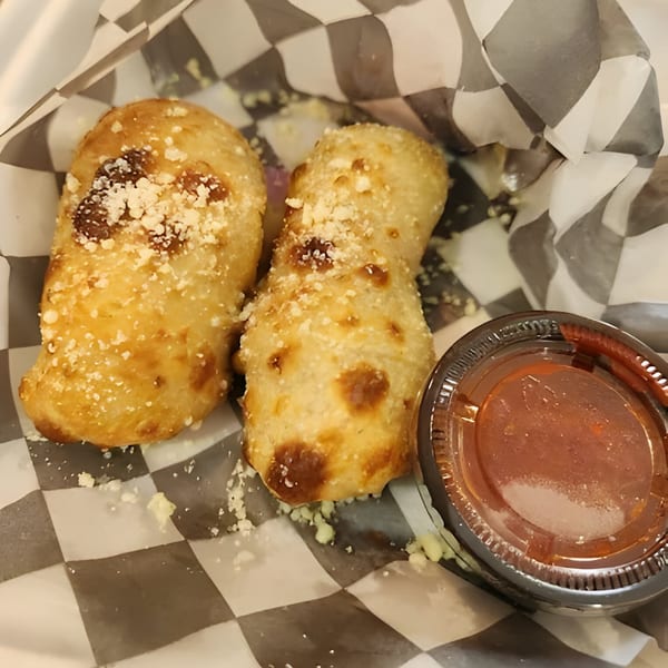 Two golden-brown Mattenga's Pizzeria garlic knots with parmesan cheese and a side of marinara sauce.