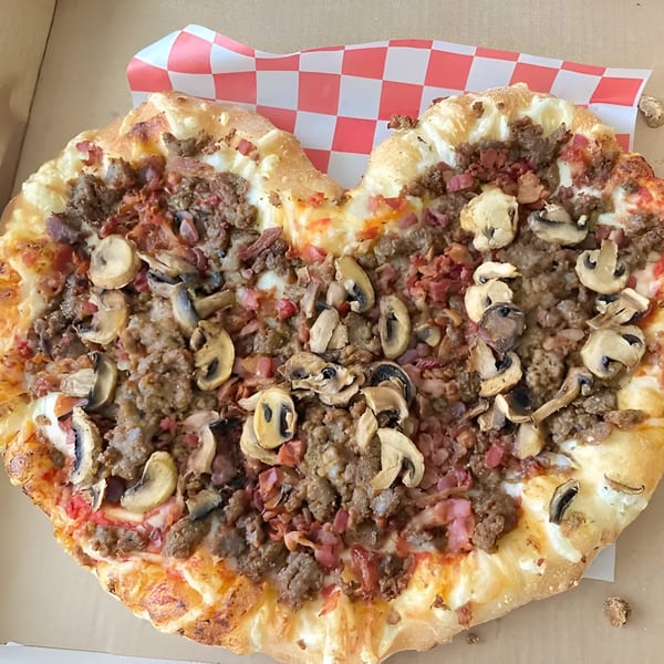 Heart-shaped Mattenga's Pizzeria pizza with sausage, bacon, and mushrooms in a delivery box.