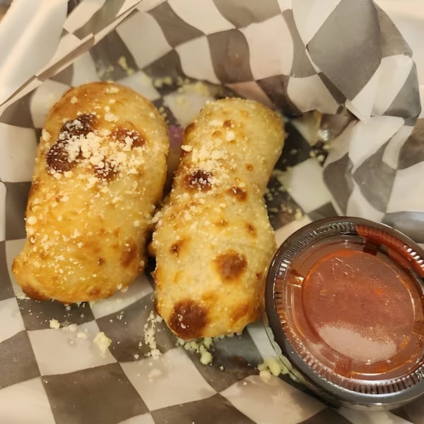 Two golden-brown Mattenga's Pizzeria garlic knots with parmesan cheese, served with marinara sauce in checkered paper.