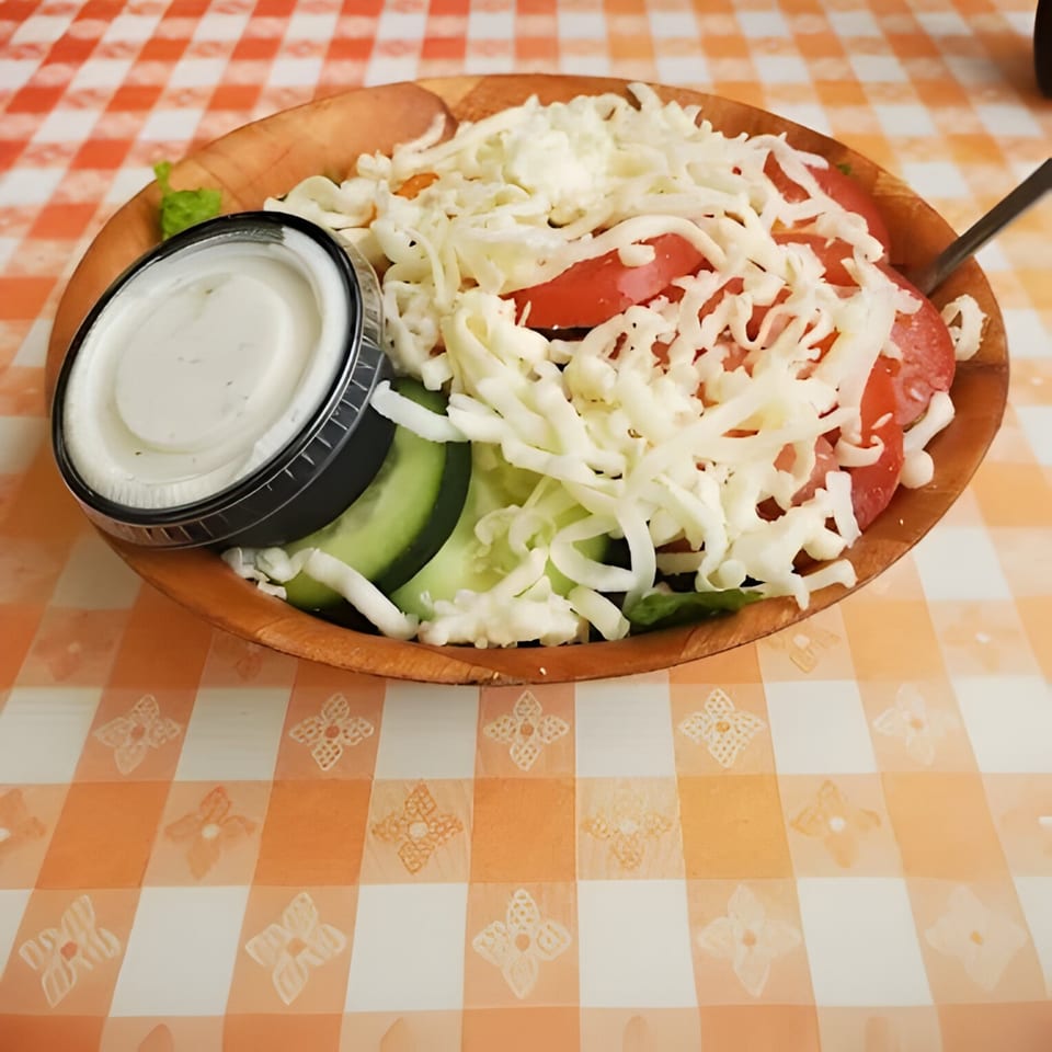 Mattenga's Pizzeria side salad with tomatoes, cucumbers, shredded cheese, and ranch dressing.