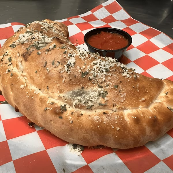 A Mattenga's Pizzeria calzone, sprinkled with herbs and cheese, served with a side of marinara sauce.