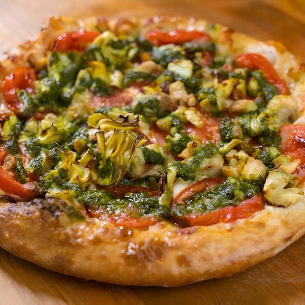 Mattenga's Pizzeria pizza with pesto, tomatoes, and artichoke hearts on a wooden surface.
