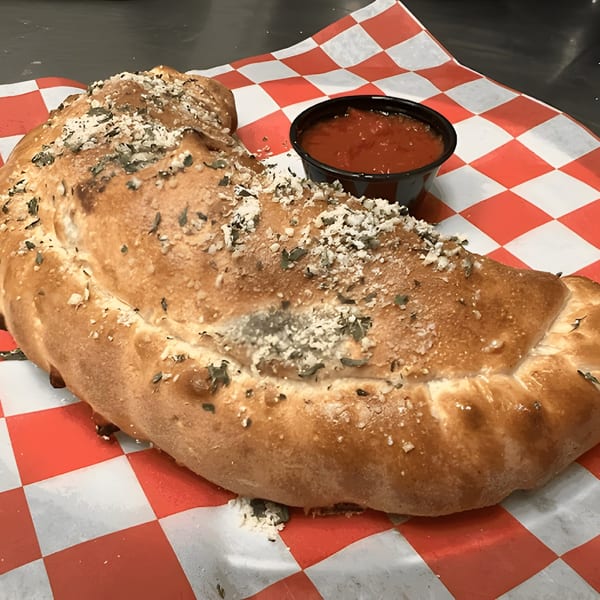 A golden-brown calzone, topped with herbs and cheese, served with a side of marinara sauce.
