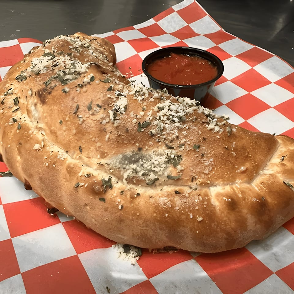 A golden-brown calzone, topped with herbs and cheese, served with a side of marinara sauce.