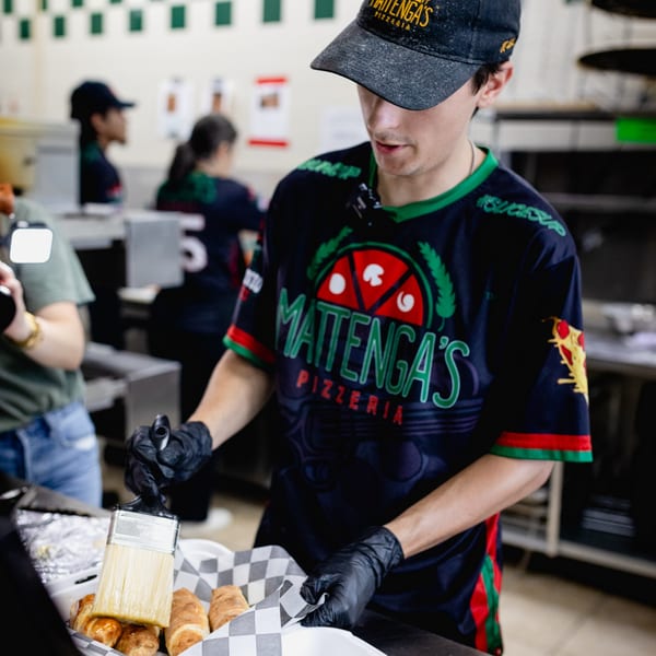 Mattenga's Pizzeria employee in uniform brushing glaze on croissants in a kitchen setting.