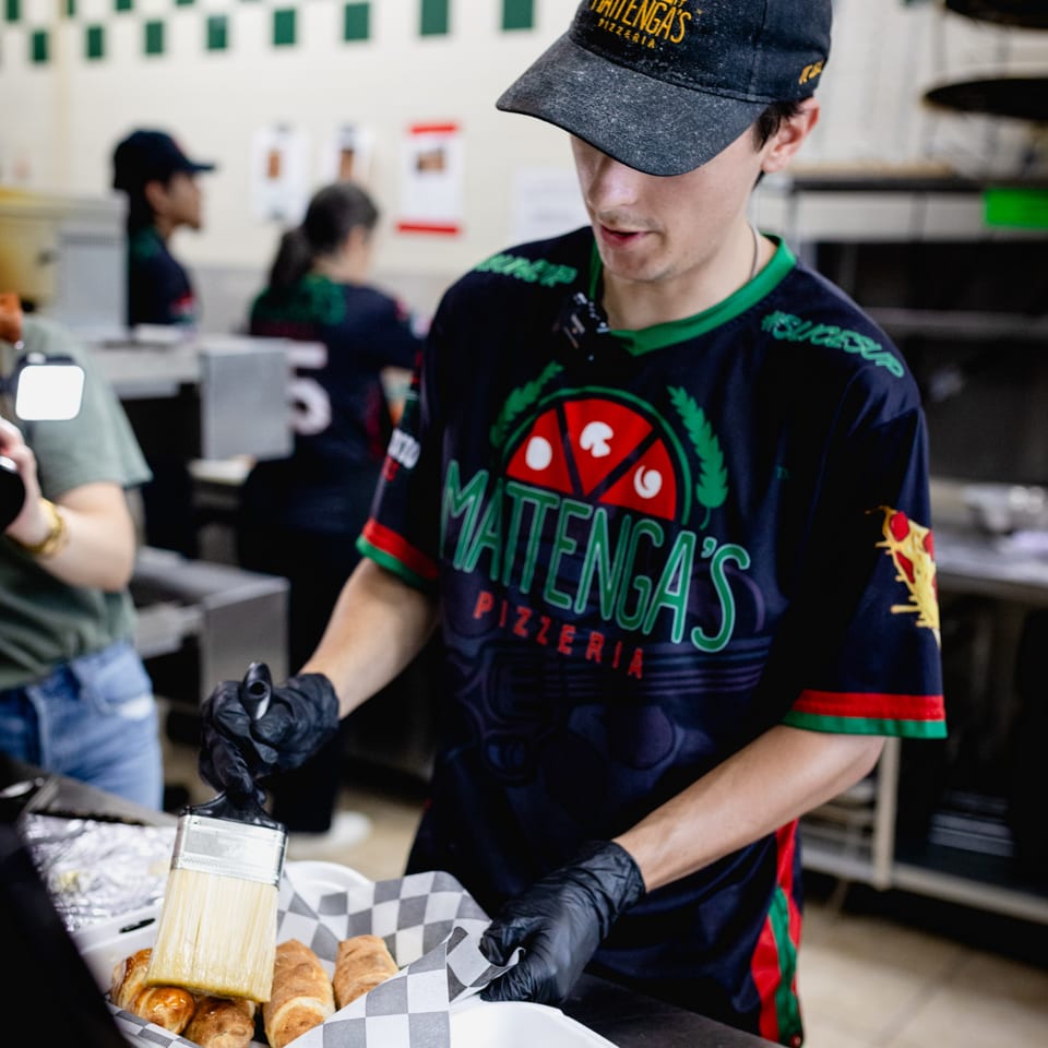 Mattenga's Pizzeria employee in uniform brushing glaze on croissants in a kitchen setting.