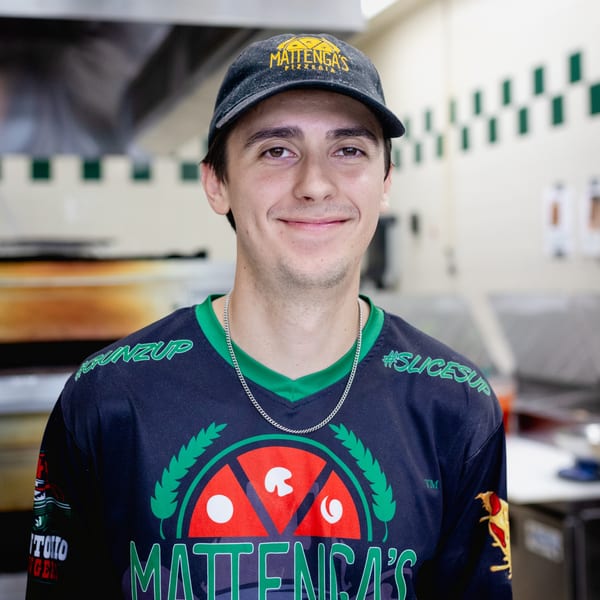 A smiling Mattenga's Pizzeria employee in uniform, wearing a branded hat and shirt.