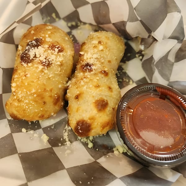 Two golden-brown Mattenga's Pizzeria garlic knots with parmesan cheese and a side of marinara sauce.